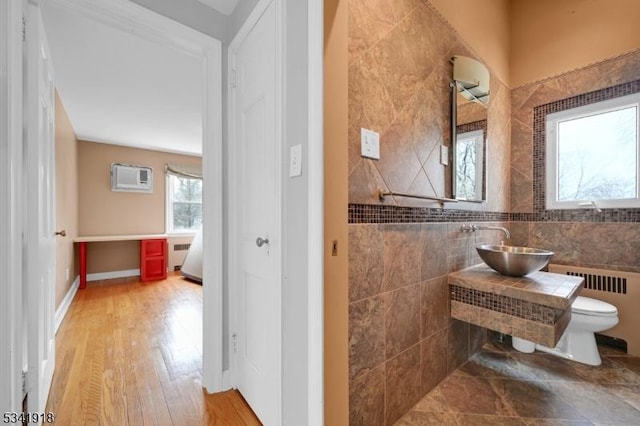 bathroom with radiator, a sink, an AC wall unit, and toilet