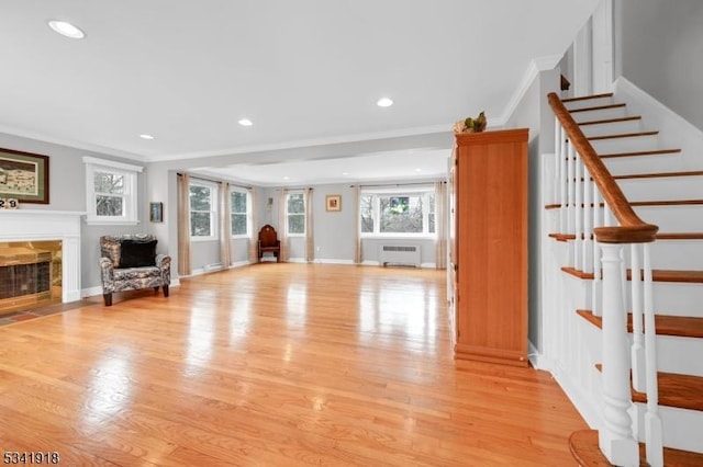 unfurnished living room with light wood-style floors, a fireplace with flush hearth, ornamental molding, and radiator heating unit