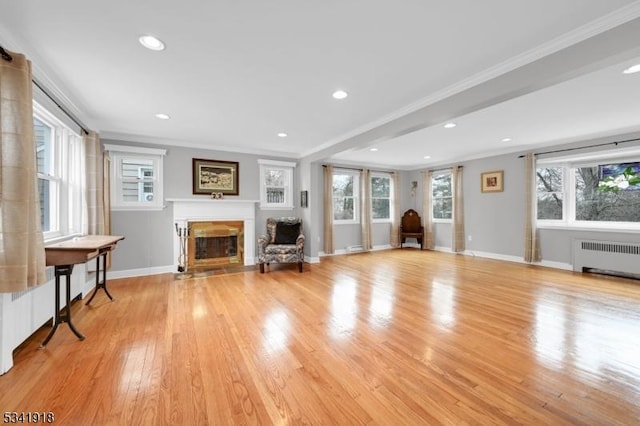 unfurnished room featuring baseboards, radiator heating unit, a fireplace with flush hearth, ornamental molding, and light wood-style floors