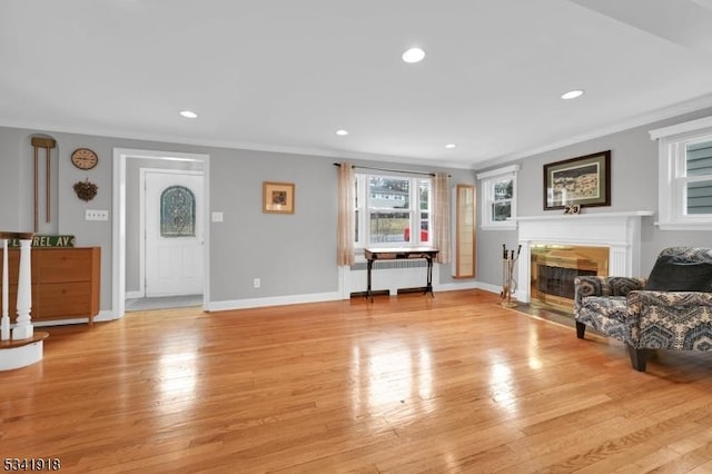 living area featuring light wood-style flooring, ornamental molding, radiator heating unit, and a fireplace with flush hearth