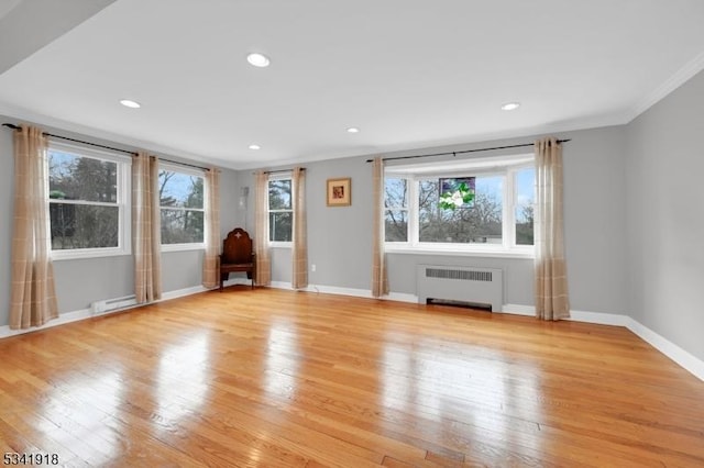 spare room featuring radiator, light wood-style floors, baseboards, and crown molding