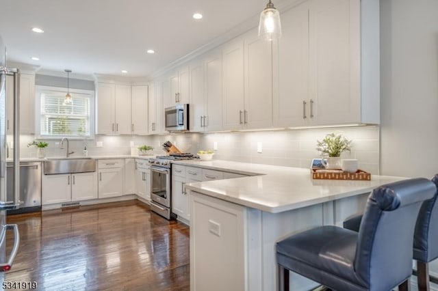 kitchen featuring appliances with stainless steel finishes, a peninsula, light countertops, white cabinetry, and pendant lighting