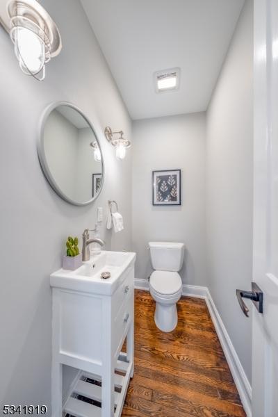 half bath featuring toilet, baseboards, wood finished floors, and vanity