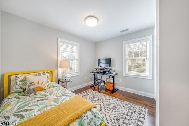 bedroom featuring multiple windows, visible vents, baseboards, and wood finished floors