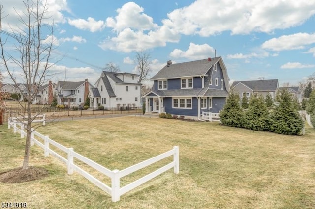 exterior space with a fenced front yard, a residential view, a gambrel roof, and a front yard