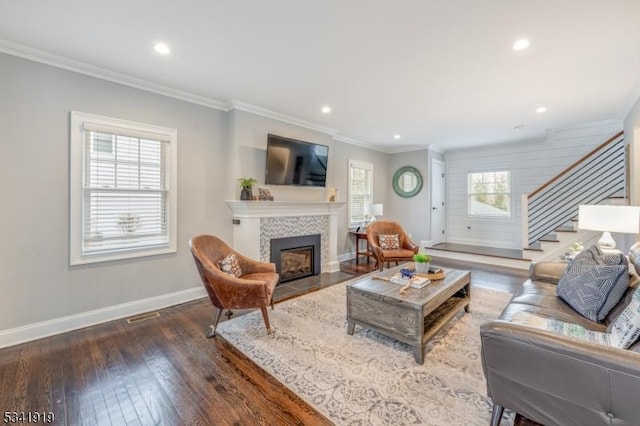 living room with crown molding, stairway, a tiled fireplace, hardwood / wood-style floors, and baseboards