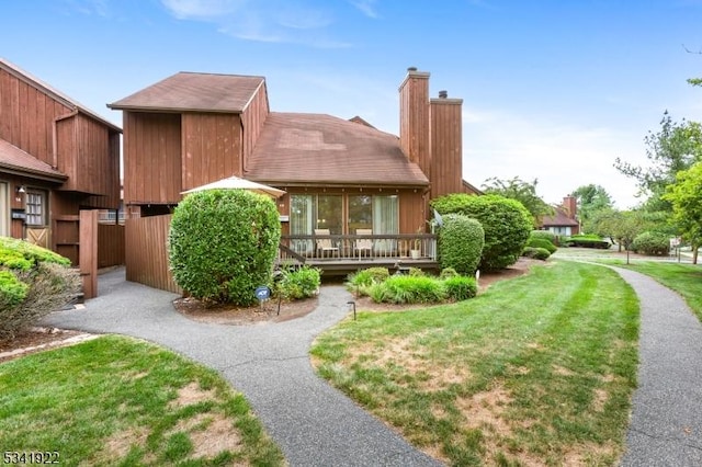 exterior space featuring a wooden deck, a chimney, and a front lawn