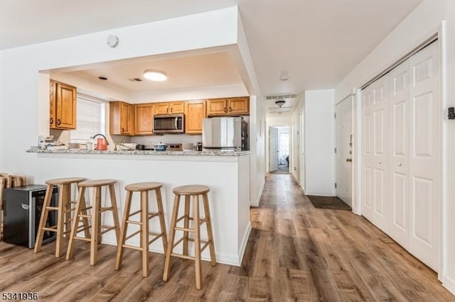 kitchen featuring wood finished floors, stainless steel microwave, a peninsula, and fridge