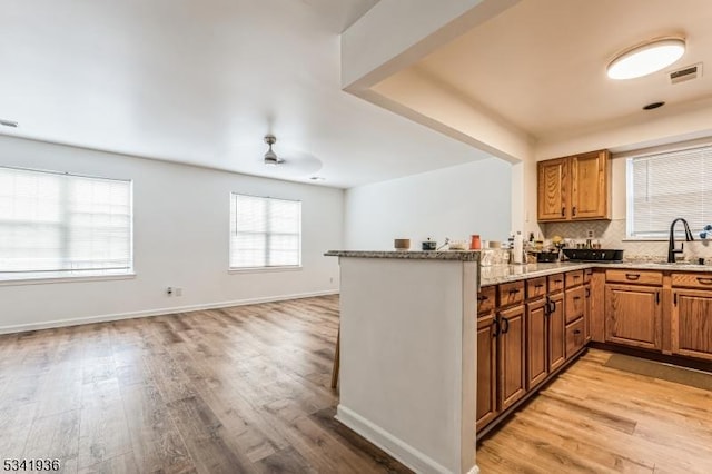 kitchen featuring tasteful backsplash, visible vents, a sink, light stone countertops, and light wood-type flooring