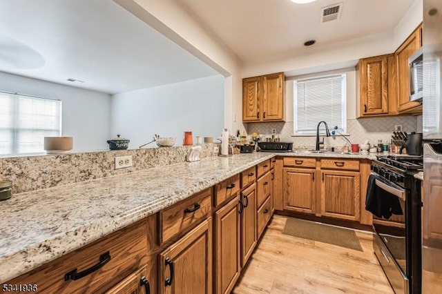 kitchen with stainless steel gas range oven, visible vents, light wood-style flooring, light stone counters, and a sink