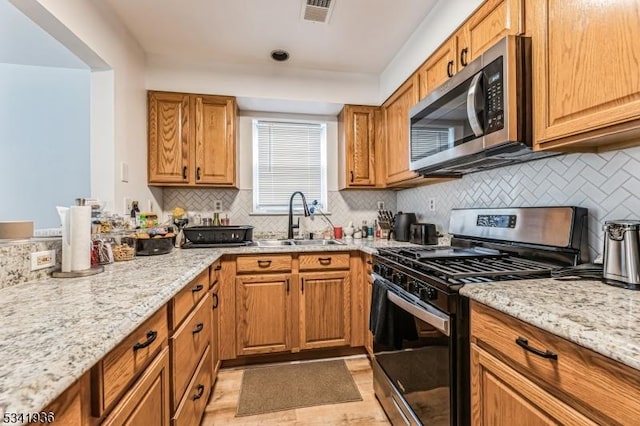 kitchen featuring light stone counters, visible vents, stainless steel appliances, and a sink