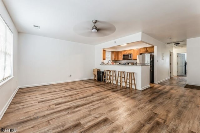 unfurnished living room with a ceiling fan, visible vents, baseboards, and wood finished floors