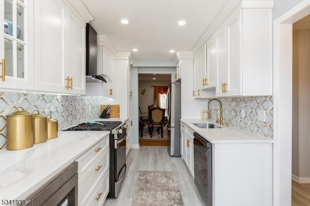 kitchen featuring stainless steel appliances, a sink, white cabinets, wall chimney exhaust hood, and light wood finished floors