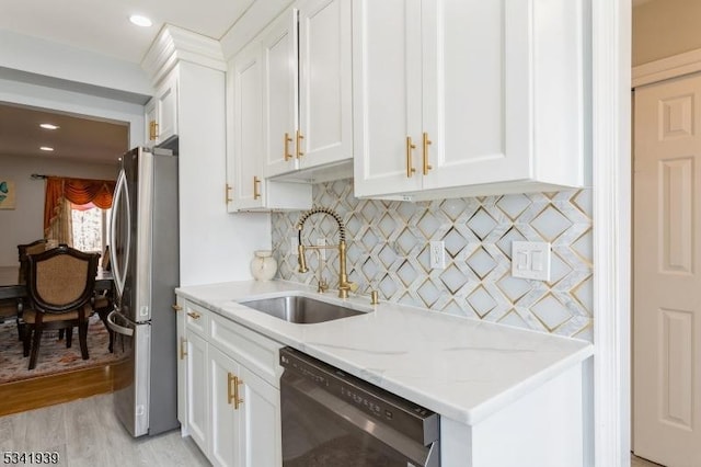 kitchen with light stone counters, freestanding refrigerator, white cabinetry, a sink, and dishwashing machine