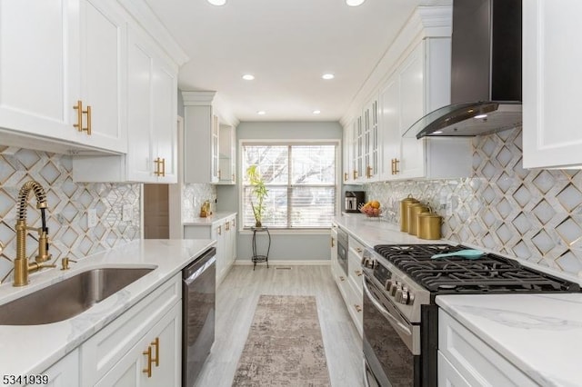 kitchen with wall chimney exhaust hood, stainless steel appliances, white cabinetry, a sink, and baseboards