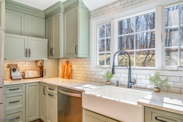 kitchen featuring light countertops, backsplash, green cabinets, a sink, and dishwasher