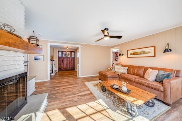 living room with a ceiling fan, a large fireplace, light wood-style flooring, and baseboards