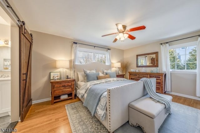 bedroom with baseboards, a barn door, ensuite bath, and light wood-style floors