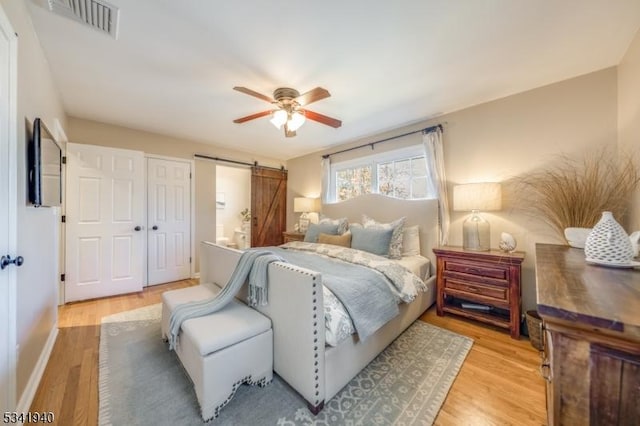 bedroom with a ceiling fan, light wood-type flooring, visible vents, and a barn door