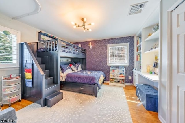 bedroom with wallpapered walls, baseboards, visible vents, wood finished floors, and an inviting chandelier