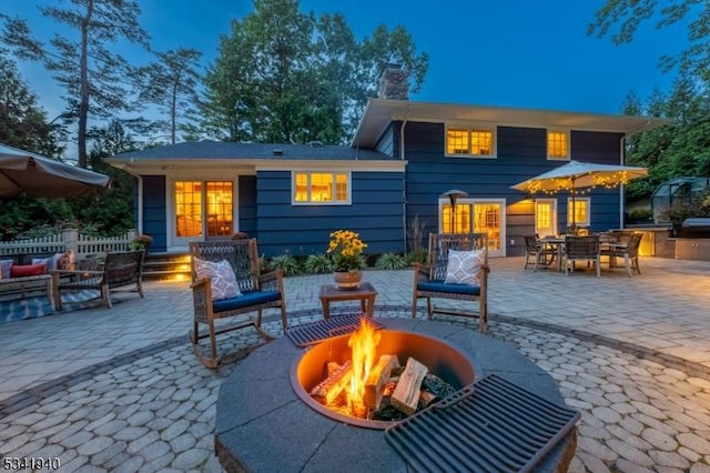 back of house featuring an outdoor fire pit, fence, outdoor dining space, a chimney, and a patio area