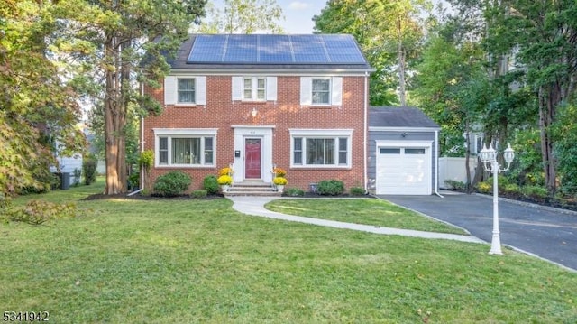 colonial-style house with brick siding, solar panels, an attached garage, driveway, and a front lawn