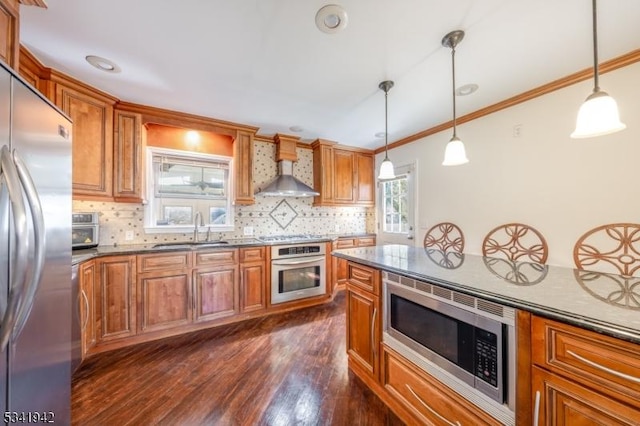 kitchen with wall chimney exhaust hood, appliances with stainless steel finishes, brown cabinetry, and a sink