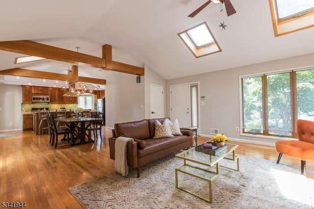 living room featuring lofted ceiling with skylight, baseboards, light wood-type flooring, and ceiling fan