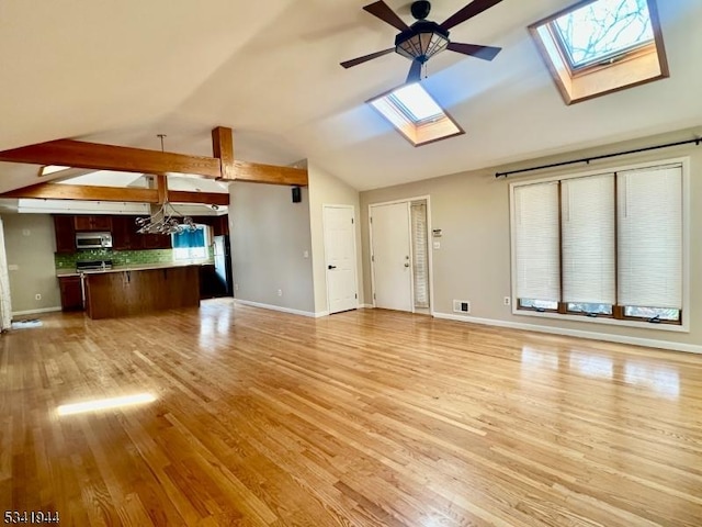 unfurnished living room featuring vaulted ceiling with skylight, baseboards, light wood-type flooring, and a ceiling fan