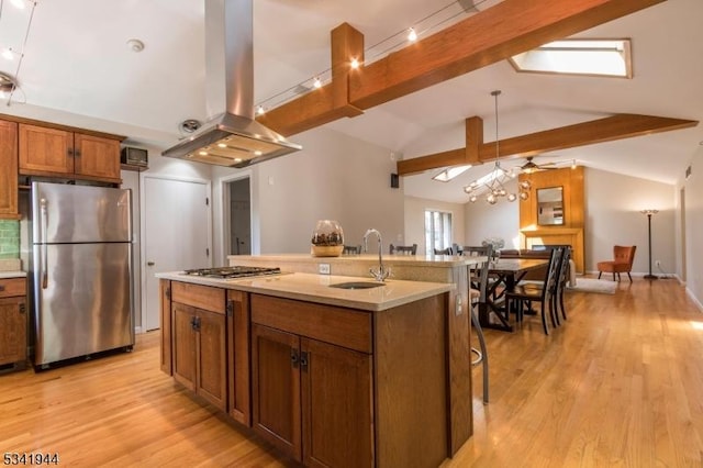 kitchen with vaulted ceiling with beams, appliances with stainless steel finishes, island exhaust hood, brown cabinetry, and a sink