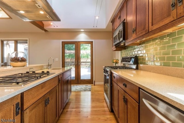 kitchen with range hood, stainless steel appliances, decorative backsplash, french doors, and brown cabinets