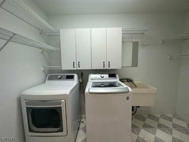 clothes washing area featuring cabinet space, washing machine and dryer, light floors, and a sink