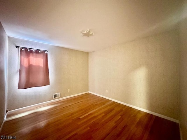 spare room featuring visible vents, baseboards, and wood finished floors