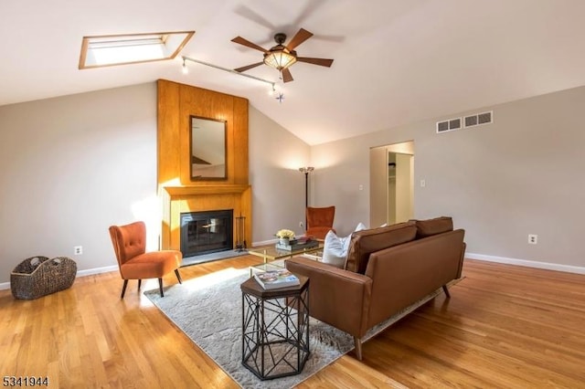 living area featuring visible vents, a ceiling fan, wood finished floors, a fireplace, and vaulted ceiling