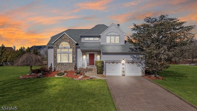 view of front of house with decorative driveway, a lawn, stone siding, and an attached garage