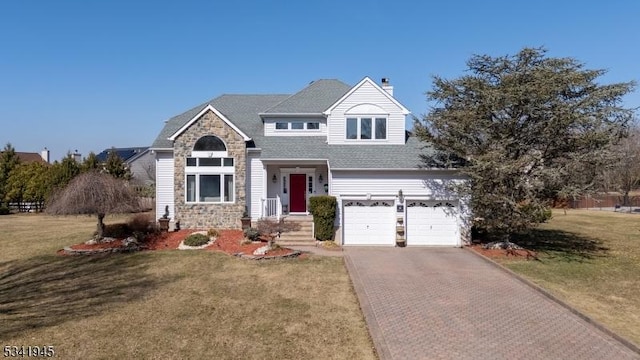 view of front of house with decorative driveway, stone siding, a front yard, a garage, and a chimney