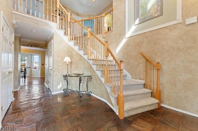 staircase featuring crown molding, stone tile floors, baseboards, and a towering ceiling