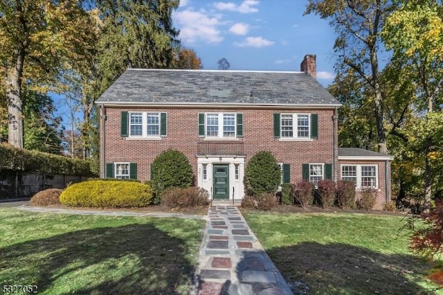 colonial inspired home featuring brick siding, a front lawn, and a chimney