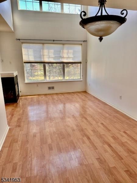 unfurnished living room featuring light wood-type flooring, visible vents, and a towering ceiling