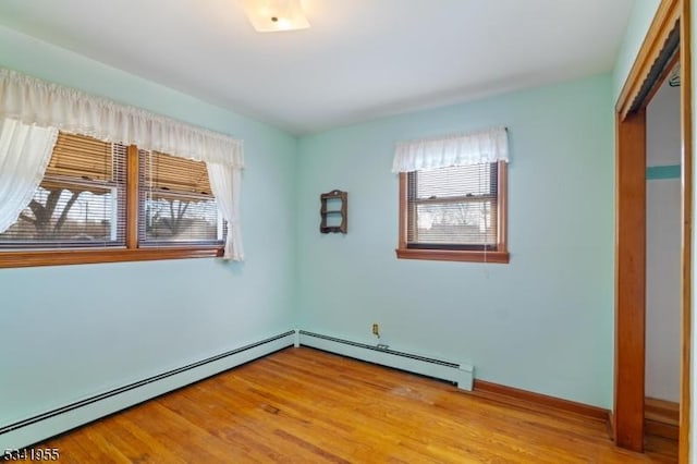 spare room with wood finished floors, a healthy amount of sunlight, baseboards, and baseboard heating