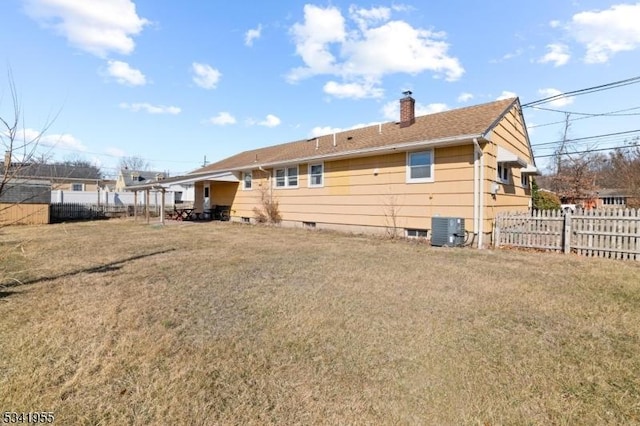 rear view of house with a yard, central AC unit, fence, and a chimney