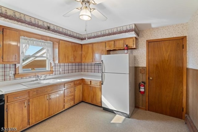 kitchen featuring a wainscoted wall, a sink, freestanding refrigerator, wallpapered walls, and light countertops