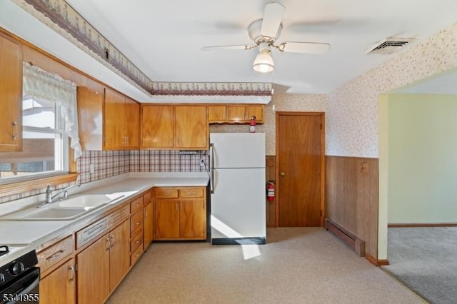 kitchen with wallpapered walls, a baseboard radiator, wainscoting, freestanding refrigerator, and a sink