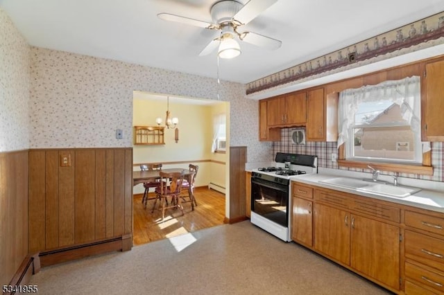 kitchen with wallpapered walls, a wainscoted wall, brown cabinets, gas stove, and a sink