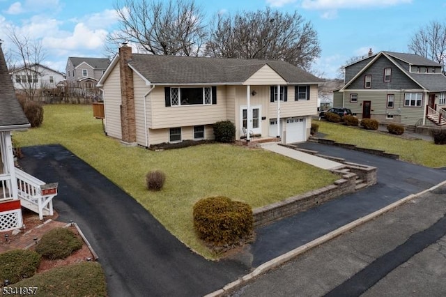 raised ranch featuring a residential view, a front lawn, a chimney, and driveway