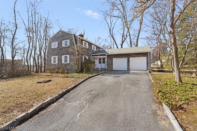 view of front of property featuring an attached garage, driveway, a chimney, and a gambrel roof