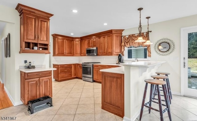 kitchen featuring a peninsula, light countertops, appliances with stainless steel finishes, brown cabinetry, and a kitchen bar