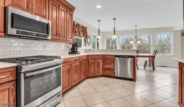 kitchen featuring stainless steel appliances, light countertops, decorative backsplash, brown cabinets, and decorative light fixtures