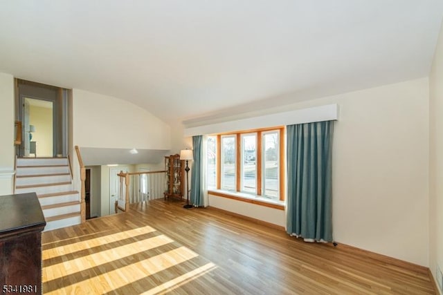 unfurnished living room with vaulted ceiling, wood finished floors, and stairs