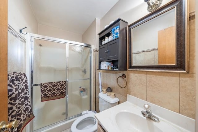 full bath featuring toilet, a shower with door, tile walls, and vanity